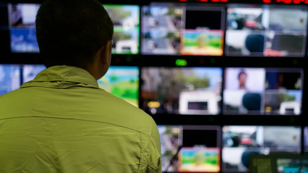 Person monitoring multiple surveillance camera feeds on multiple screens.